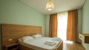 A bedroom with a wooden bed, a nightstand, a hanging light fixture, and a window with curtains. - SanPietro Vacation Apartment 033 (Durrës)