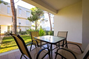 Eine Terrasse mit Glastisch und -stühlen, umgeben von einer Rasenfläche und Bäumen, mit einem Gebäude im Hintergrund.