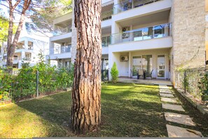 A multi-story residential building with balconies, a grassy courtyard, and a tree in the foreground. - SanPietro Vacation Apartment 033 (Durrës)