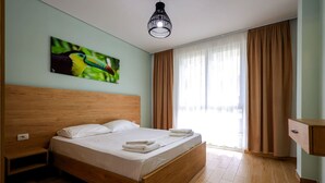Ein Schlafzimmer mit einem hölzernen Bett, einem Nachttisch, einem Papageienporträt, einem Fenster mit Vorhängen und einer Hängeleuchte.