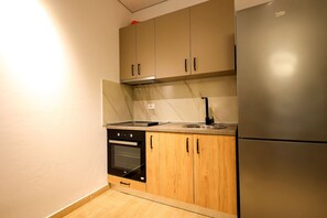 Eine kompakte Küche mit Einbauofen, Edelstahlkühlschrank und Holzschränken.