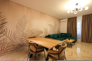 Ein modernes Wohnzimmer mit einem Holzesstisch, zwei Stühlen, einem grünen Sofa und einem kleinen Couchtisch.