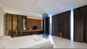 Moderni hotellihuone, jossa on suuri sänky, puinen vaatekaappi, työpöytä tietokoneella sekä suuri ikkuna, jossa on verhot.