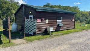 A small, single-story building with a metal roof and wooden siding, featuring a 'WOMEN' sign and a 'MEN' sign on the side. - Musician’s Glamping Cabin Near Allegany State Park & Ellicottville (Hinsdale)