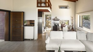 Ein modernes Wohnzimmer mit Holzbalkendecke, einem weißen Sofa und einem Essbereich mit Tisch und Stühlen.
