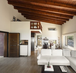 Ein modernes Wohnzimmer mit Holzbalkendecke, einem weißen Sofa und einem Essbereich mit Tisch und Stühlen.