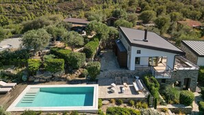 Ein modernes Haus mit Swimmingpool, umgeben von üppiger Vegetation und Hügeln.