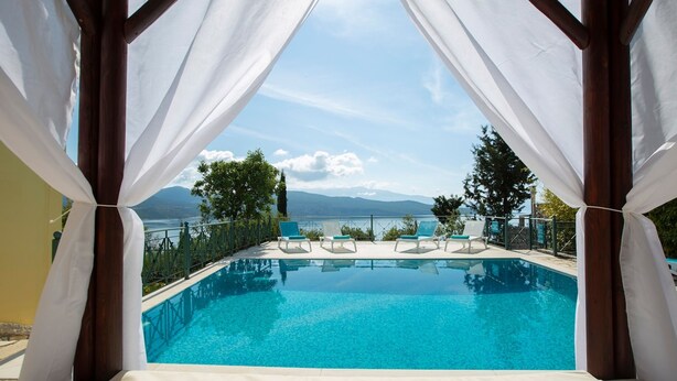 A clear view of a swimming pool with a mountain backdrop, surrounded by white curtains and lounge chairs. - Buena Vista Villa - Amazing sea view (Ligia)