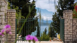 A stone gate with a metal fence leading to a body of water, surrounded by trees and a mountain in the background. - Buena Vista Villa - Amazing sea view (Ligia)