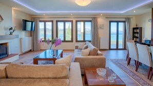 A spacious living room with a sofa set, a coffee table, and a view of the sea through large windows. - Buena Vista Villa - Amazing sea view (Ligia)