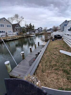 A dock extending into a calm river, surrounded by residential houses and a white picket fence.