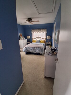 A bedroom with a bed, a nightstand, a dresser, a ceiling fan, and a window with a curtain.