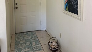A hallway with a white door, a framed painting of a bird, a patterned rug, and a basket of seashells. - Well kept condo in Fort Myers on an executive golf course and view of first hole (Fort Myers)