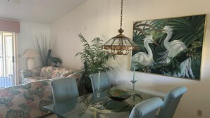 A dining area with a glass table, chairs, a chandelier, a painting of a bird, and a sofa with floral upholstery. - Well kept condo in Fort Myers on an executive golf course and view of first hole (Fort Myers)