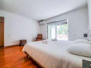 Ein Schlafzimmer mit Bett, einem Sessel, einem kleinen Tisch und einem Fenster mit Blick ins Grüne.