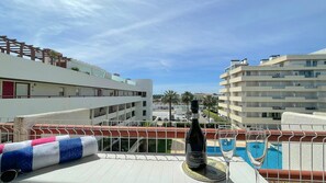 A balcony with a bottle of wine, a pool, and buildings in the background. - Poolside Bliss | T1 HsRentals Vilamarina (Vilamoura)