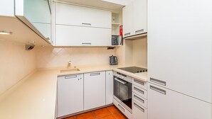 A compact kitchen with white cabinetry, a built-in oven, and a coffee maker. - Onde a Marina é Casa | T2 HsRentals Vilamarina (Vilamoura)