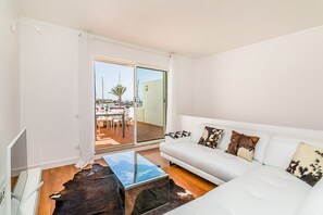 Un salón moderno con un sofá blanco, una mesa de centro de vidrio y vistas al exterior.