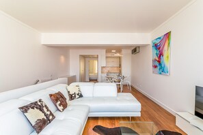 A modern living room with a white sectional sofa, a glass coffee table, and a flat-screen TV. - Onde a Marina é Casa | T2 HsRentals Vilamarina (Vilamoura)