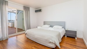 A bedroom with a bed, a bedside table, a nightstand, and a sliding glass door leading to an outdoor area. - Onde a Marina é Casa | T2 HsRentals Vilamarina (Vilamoura)