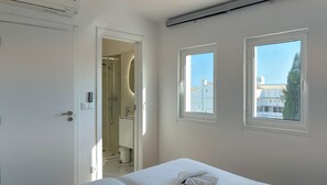 A bedroom with a bed, a shower, and two windows with a view of buildings. - Vila Shradhala | V4 HsR Marina Vilamoura (Vilamoura)