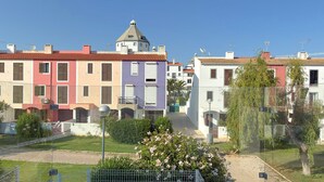 A row of colorful buildings with a central tower, a small garden with flowers, and a clear sky. - Vila Shradhala | V4 HsR Marina Vilamoura (Vilamoura)