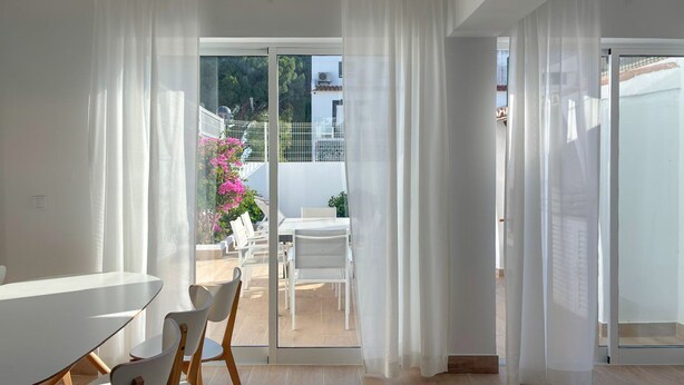 A modern interior with a dining area, white curtains, and a view of an outdoor patio with chairs and a table. - Vila Shradhala | V4 HsR Marina Vilamoura (Vilamoura)