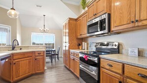 A kitchen with wooden cabinets, stainless steel appliances, a granite countertop, and a chandelier.