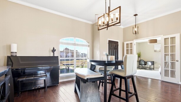 A spacious living room with a piano, a dining table with chairs, and a large window offering a view of the outdoors.