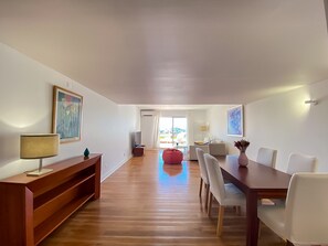 Un salon moderne avec un plancher en bois, une table à manger avec des chaises, un fauteuil poire rouge et des œuvres d’art accrochées aux murs.