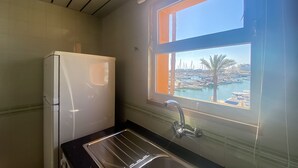Ett kök med kylskåp, diskho och ett fönster med utsikt över en småbåtshamn.