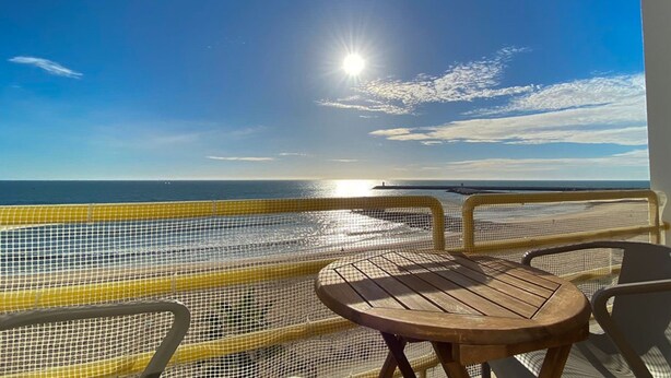 Ein Balkon mit Blick auf das Meer, einem Holztisch und zwei Stühlen.