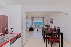 Eine moderne Küche mit roter Arbeitsplatte, einer Kaffeemaschine und einem Geschirrspüler. Es gibt einen Essbereich mit Tisch und Stühlen sowie Meerblick durch große Fenster.