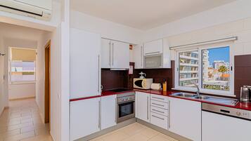 A modern kitchen with white cabinets, a red countertop, a built-in microwave, a toaster, a sink, and an oven.
