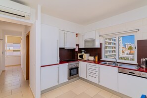 Eine moderne Küche mit weißen Schränken, einer roten Arbeitsplatte, einer eingebauten Mikrowelle, einem Toaster, einer Spüle und einem Backofen.