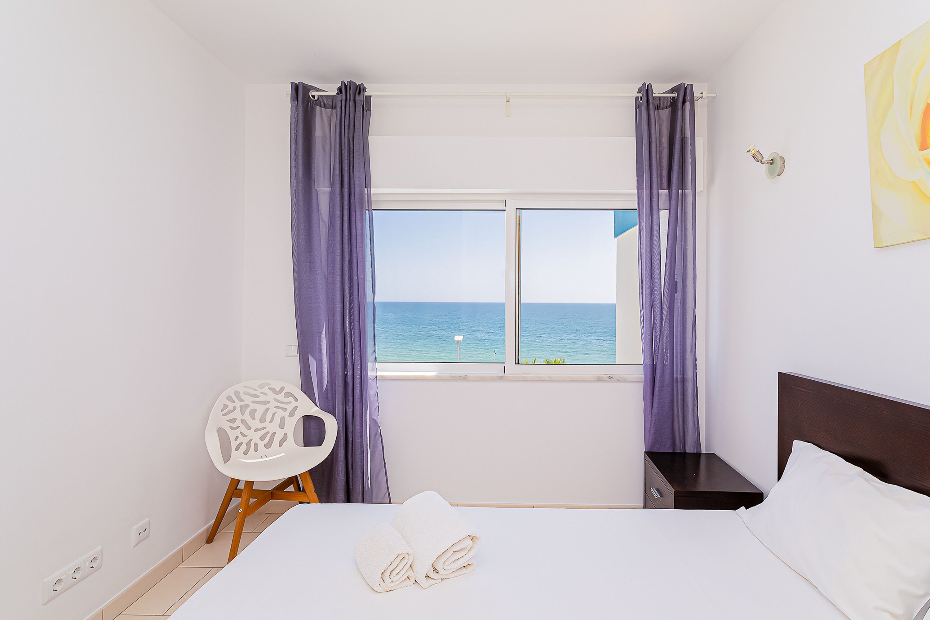 A bedroom with a bed, a chair, a nightstand, and a window with curtains.