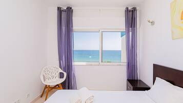 A bedroom with a bed, a chair, a nightstand, and a window with curtains.
