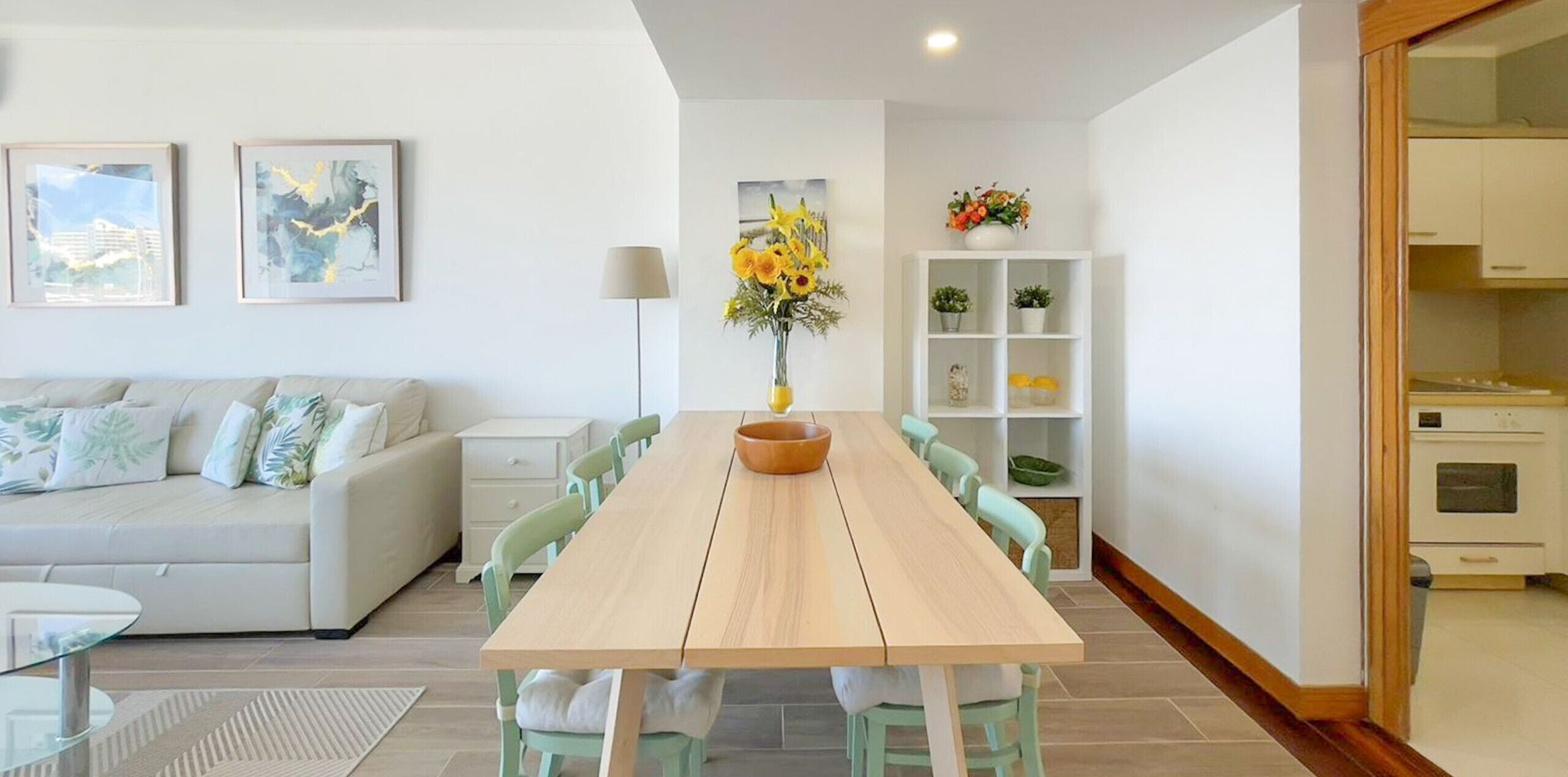 A modern living room with a wooden dining table, light-colored sofa, and a white cabinet with shelves.