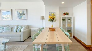 Una sala de estar moderna con una mesa de comedor de madera, un sofá de colores claros y un mueble blanco con estantes.