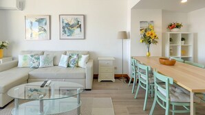 Una sala de estar moderna con un sofá, una mesa de centro de vidrio, una mesa de comedor con sillas y obras de arte en las paredes.