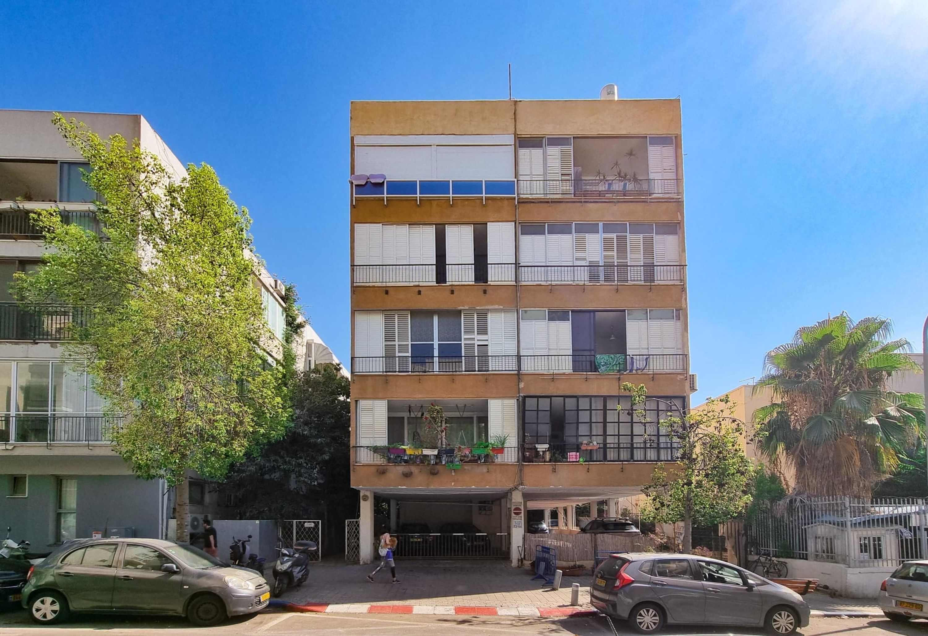A multi-story building with balconies, a covered entrance, and parked cars.