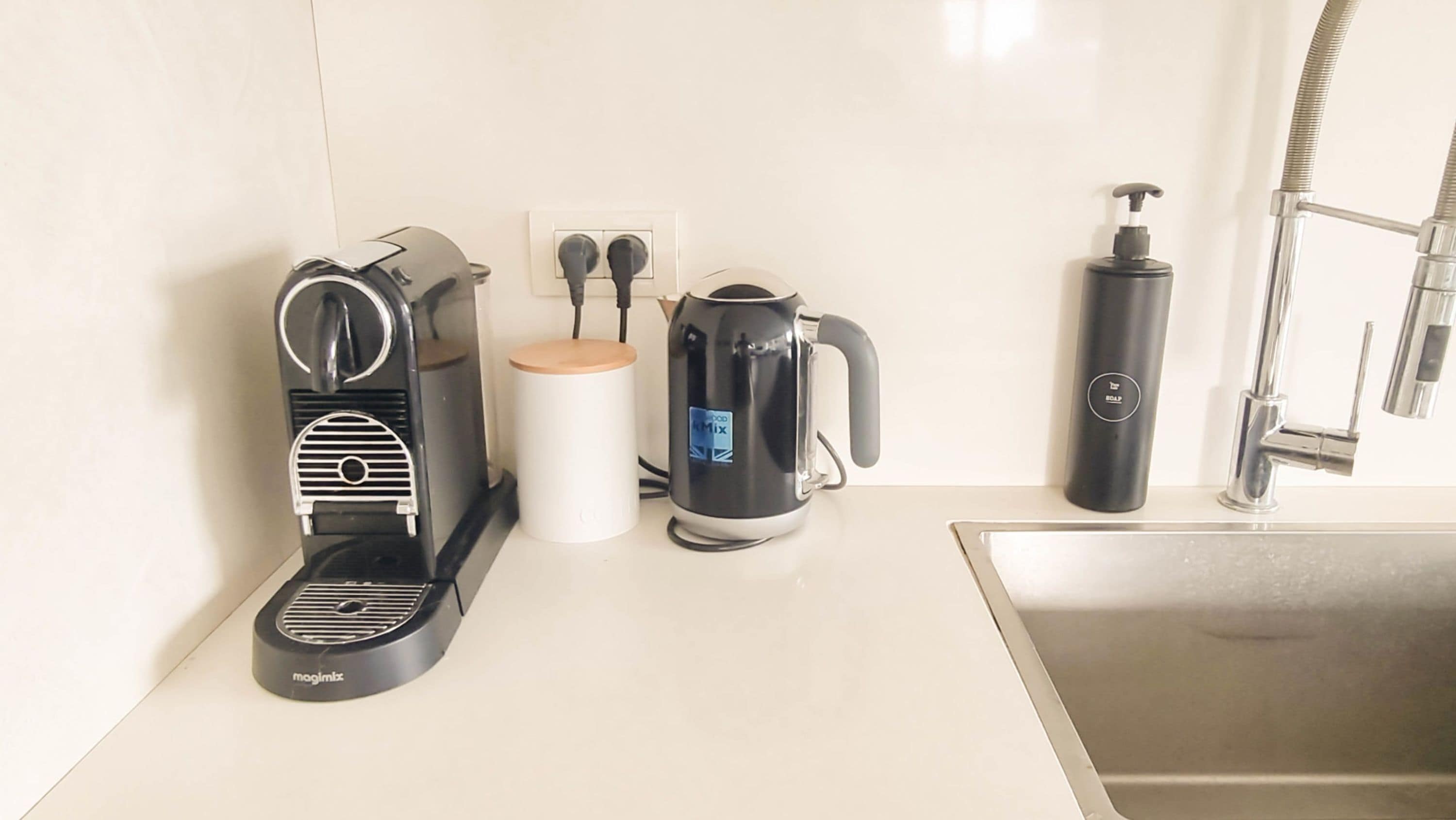 A kitchen with a coffee maker, a kettle, a soap dispenser, and a faucet.