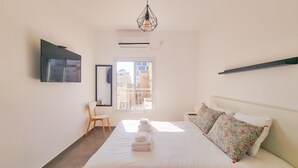 A bedroom with a bed, a chair, a TV, a window, and an air conditioning unit. - Geula Tulipe in Tel Aviv-Yafo (Tel Aviv-Yafo)