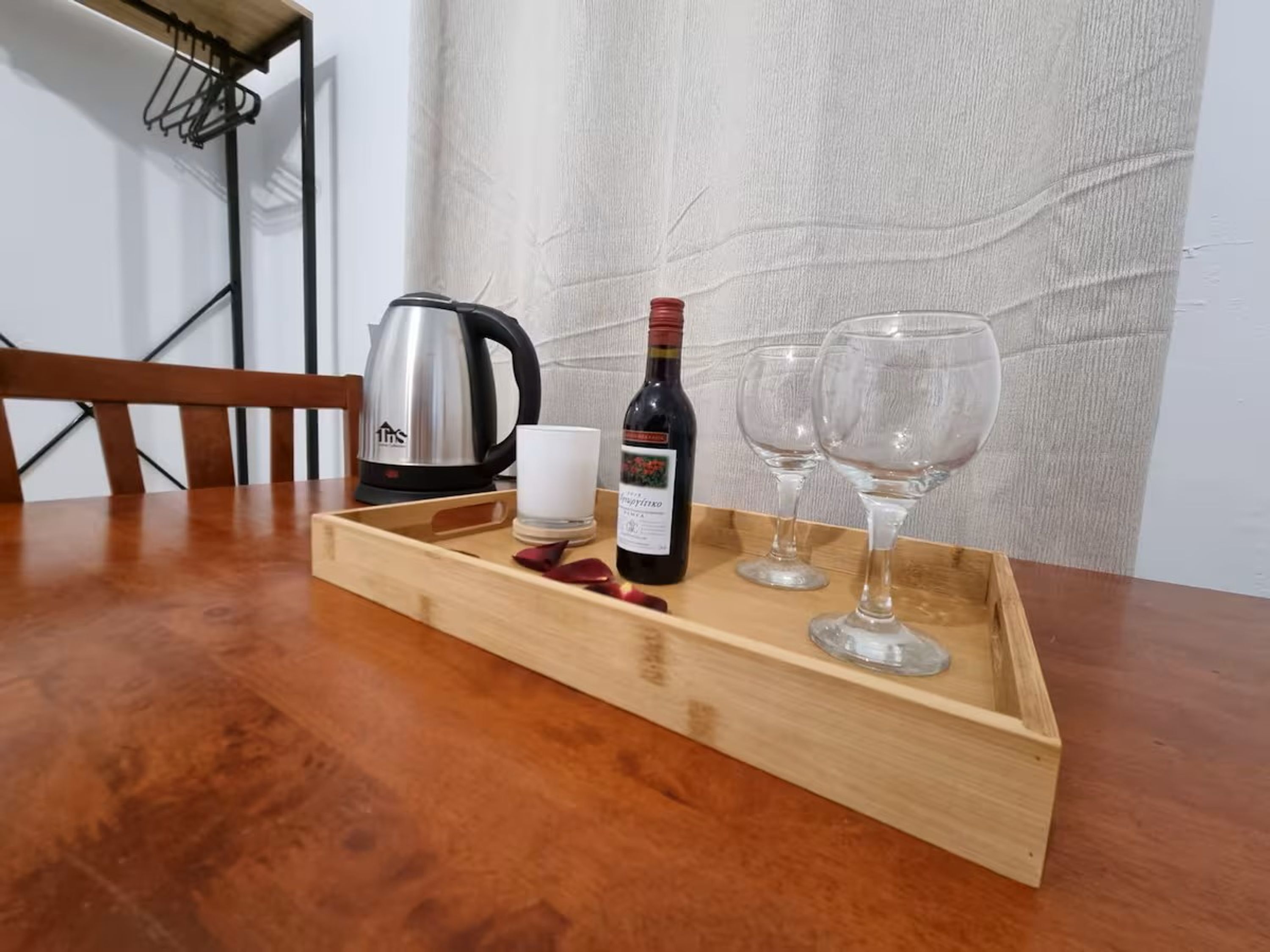 A wooden tray with a wine bottle, two glasses, and a candle on a wooden table.