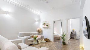 Uma sala de estar moderna com sofá, mesa de centro e televisão. Há uma planta e uma prateleira na parede com objetos decorativos.