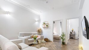 A modern living room with a sofa, a coffee table, and a TV. There is a plant and a wall-mounted shelf with decorative items. - VISIT_GENOVA NEW FAMILY APARTMENT, 4 BEDROOMS-Visit_Genova (Genova)