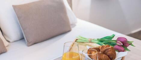 A breakfast tray with croissants, juice, and tulips on a wooden table in a hotel room.