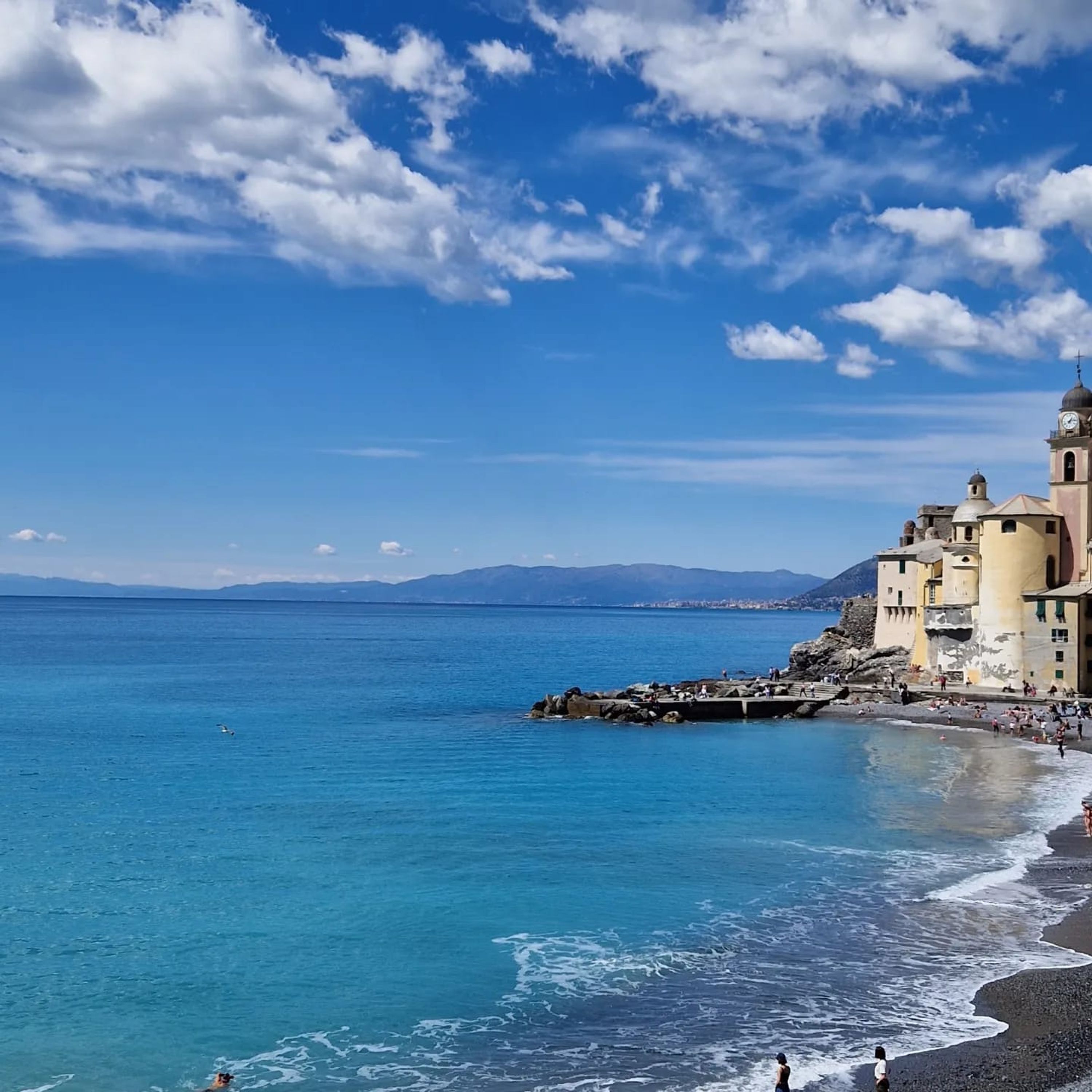 A coastal town with a prominent church, clear blue sea, and rocky shoreline.