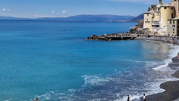 Uma vila costeira com uma igreja imponente, mar azul cristalino e costa rochosa.