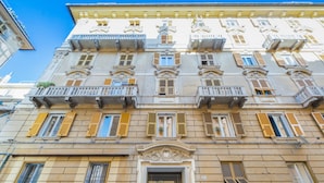 Um edifício de vários andares com estilo arquitetônico clássico, apresentando varandas, grandes janelas e uma entrada central.